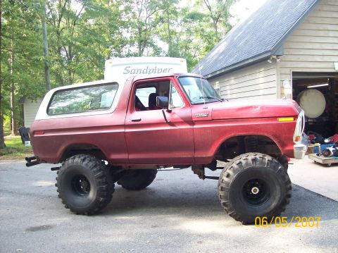 1978 Ford Bronco - This lifted 1978 Ford Bronco, painted red with a white top, sits parked in front of a garage.