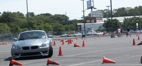 2001 Mercury Grand Marquis - A silver BMW Z4 coupe is seen on a race course with orange cones and other vehicles in the background.