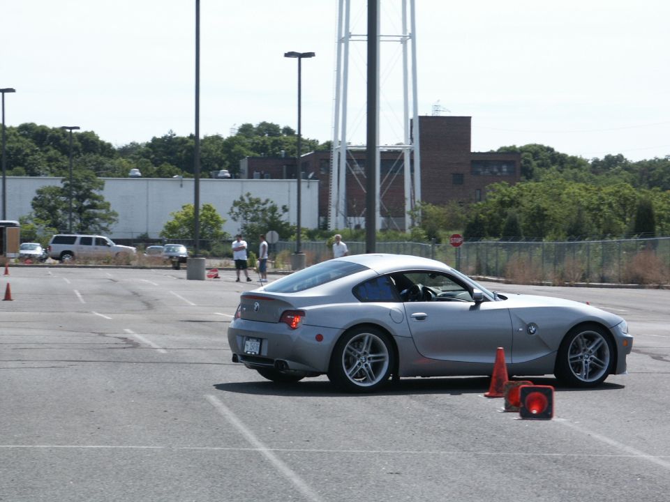 Silver BMW coupe driving through cones in a parking lot. Water tower in background