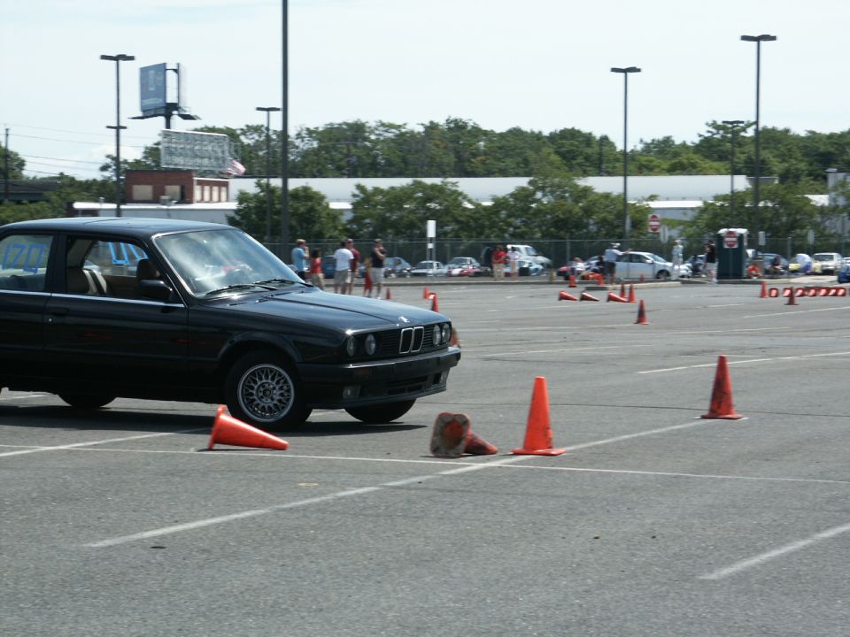 Black BMW E30 sedan navigating an autocross course with orange cones