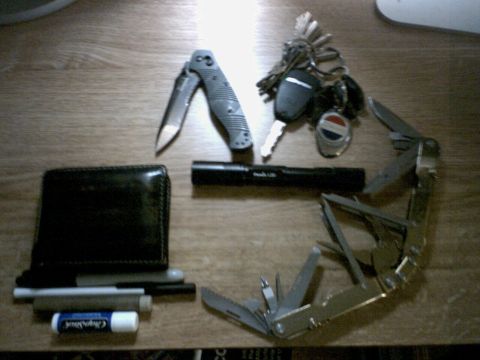 2001 Ford Crown Victoria - A collection of everyday carry items including a wallet, folding knife, flashlight, keys, and a multi-tool are arranged on a table.