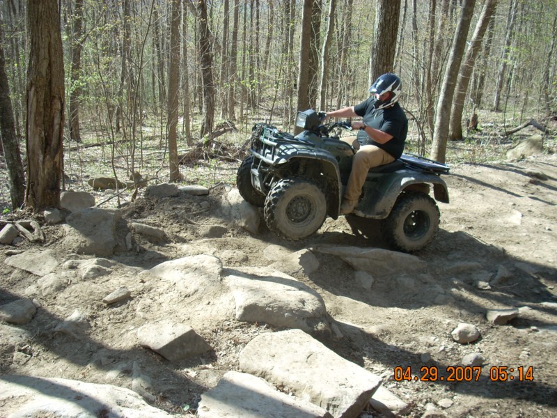 Rider on a green ATV quad climbing a rocky trail in the woods