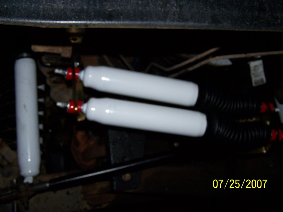 Two white shock absorbers with red accents and black bellows attached to a vehicle's undercarriage