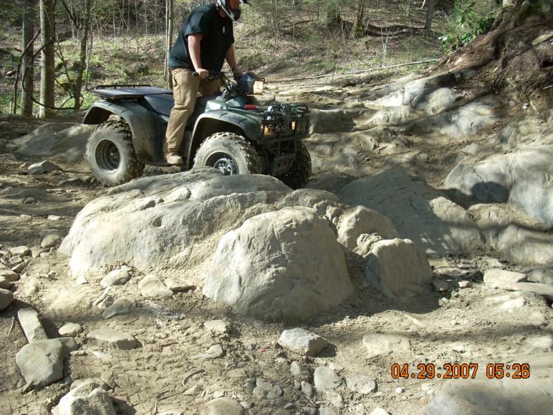 Green Honda ATV with rider crossing rocky wooded trail