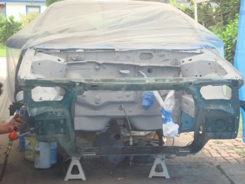 1993 Ford Taurus - Vehicle chassis undergoing preparation for a paint job, with a spray gun visible in the foreground.