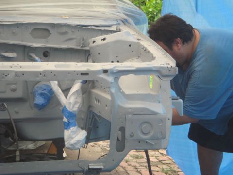 1993 Ford Taurus - A person works on the exposed engine bay of a car, which is covered in primer and masking tape.