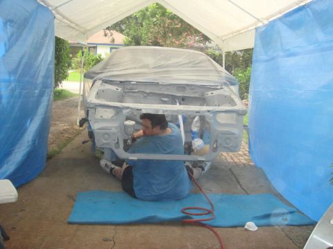 1993 Ford Taurus - A person works on a car chassis inside a tent, with blue tarps on the sides.