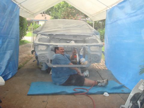 1993 Ford Taurus - A person works on the front end of a car body, which is covered by a tarp and situated under a temporary shelter.