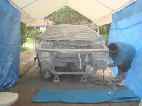 1993 Ford Taurus - A person works on the front end of a car body that is covered in plastic sheeting and supported by jack stands.