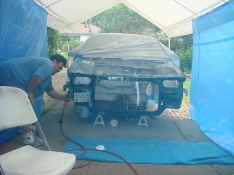 1993 Ford Taurus - A man spray paints the front end of a car body that is covered in plastic sheeting.
