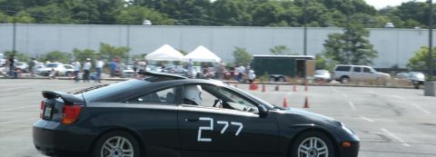 2001 Mercury Grand Marquis - A black sports car with the number 277 is seen on a race track with other vehicles and tents in the background.