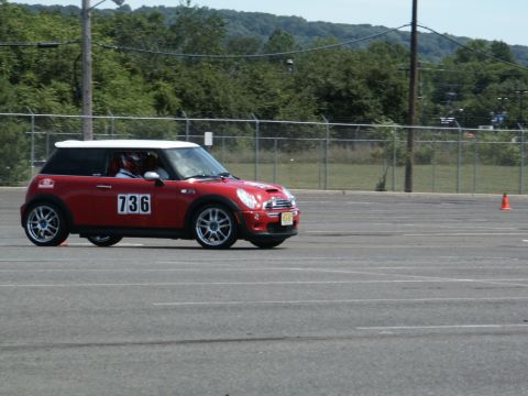 2001 Mercury Grand Marquis - A red Mini Cooper is seen on a paved surface, possibly during a timed event, with trees and a fence in the background.