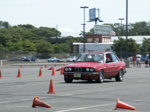 2001 Mercury Grand Marquis - A red BMW E30 coupe navigates an autocross course marked by orange cones under a bright sky.