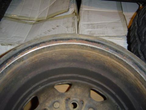 1979 Ford Bronco - A close-up view of a corroded wheel rim, with a tire and stacked boxes visible in the background.