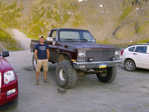 1982 Chevrolet C/K Pickup - A lifted brown pickup truck is parked next to a white SUV with a man standing beside the truck.