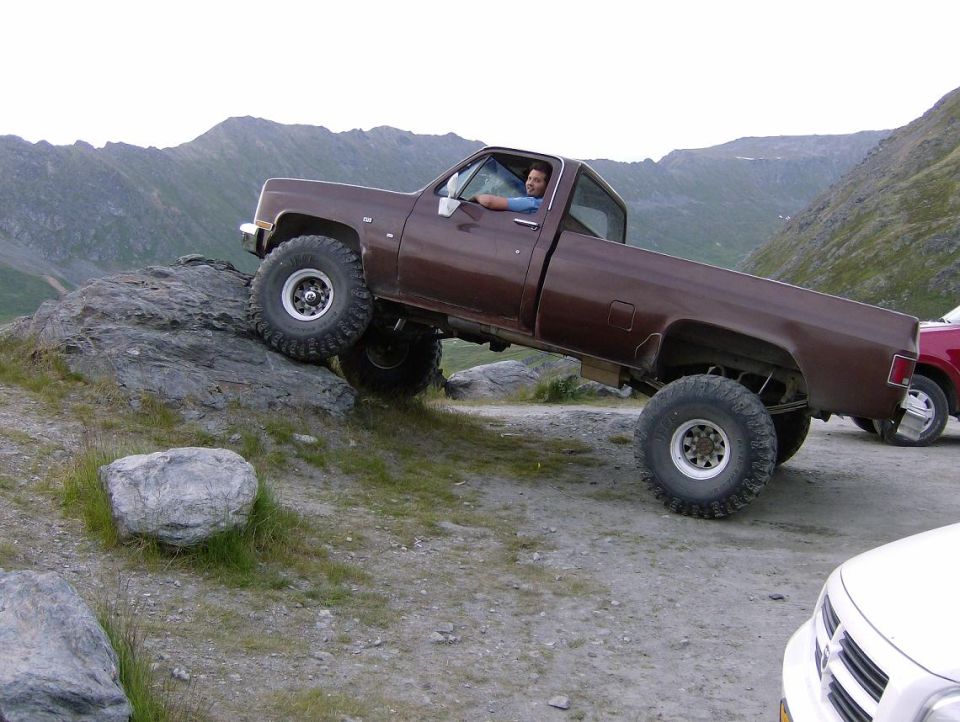 Brown 1982 Chevrolet C/K Pickup climbing a rocky incline with a driver inside
