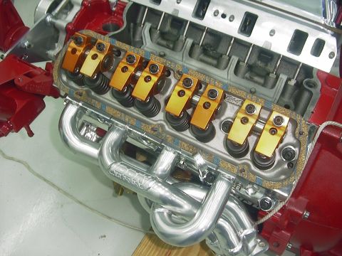 1990 Ford Mustang - Close-up view of an engine gold roller rockers and polished chrome headers, with visible text on the headers.