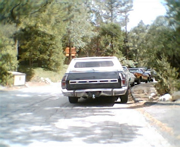 1972 Ford Ranchero - A 1972 Ford Ranchero with a camper shell is parked on a dirt road, with other vehicles visible in the background.