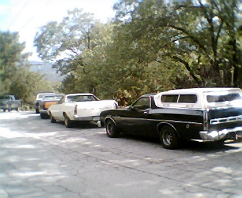 1972 Ford Ranchero - A line of classic pickup trucks, including a black 1972 Ford Ranchero with a white camper shell, parked on a roadside.