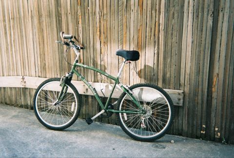1991 Ford Bronco - A green Eddie Bauer bicycle is parked next to a weathered wooden fence.