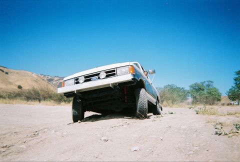 1991 Ford Bronco - A Ford F-Series truck is driving on a dirt road with hills in the background.