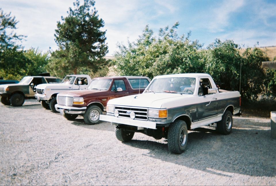 Two-tone gray and white lifted Ford Bronco on gravel with three more Broncos lined up behind