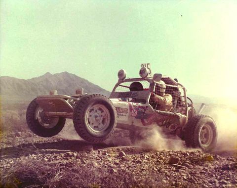 1996 Ford Bronco - Desert racing buggy airborne over rocky terrain, with mountains in the background.