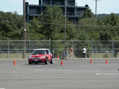 2001 Mercury Grand Marquis - A red Mini Cooper drives through an autocross course marked by orange cones, with spectators watching in the background.