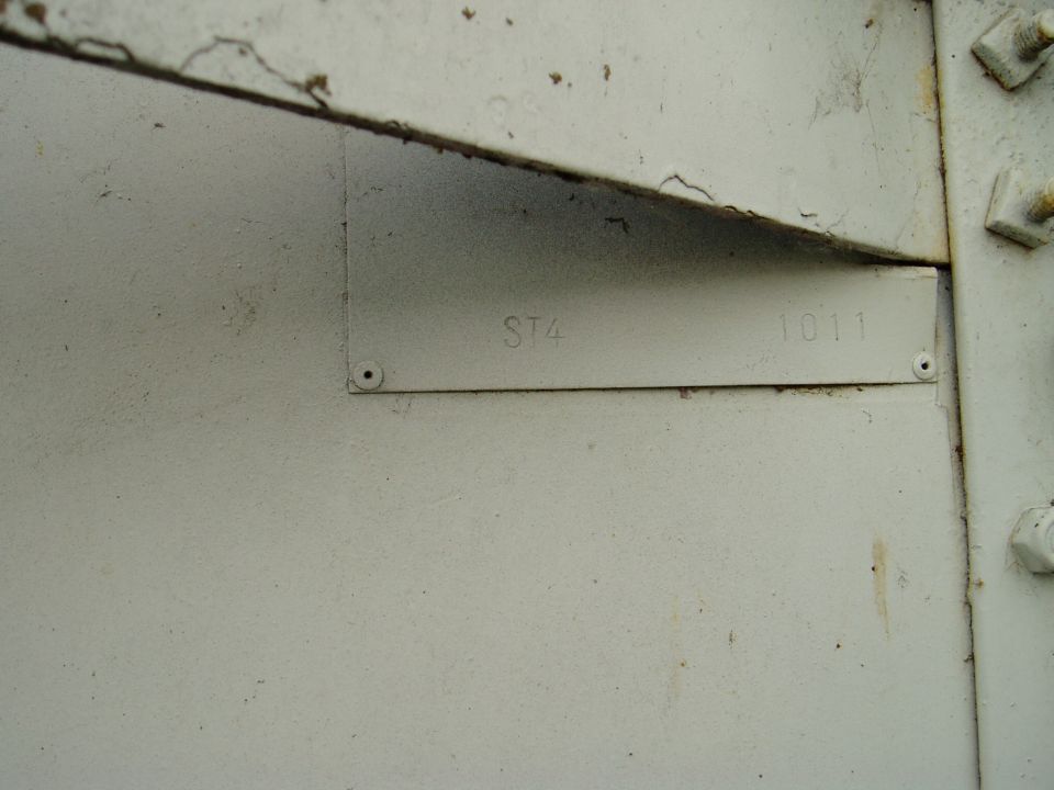 Close-up of a metal plate stamped with ST4 and 1011, attached to a painted surface