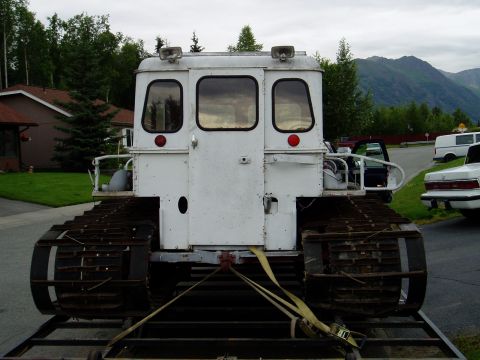 2000 Ford E350 - A white snowcat vehicle is seen from the rear, loaded onto a trailer with other vehicles in the background.