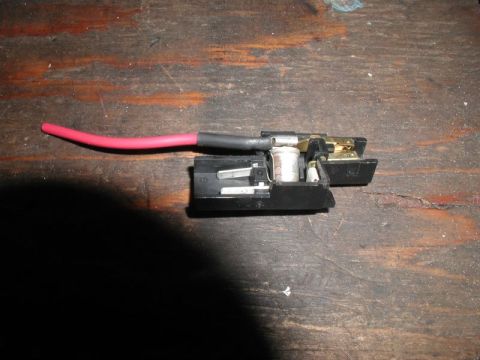 1990 Ford Thunderbird - A close-up view of a car's battery terminal connector with a red wire, placed on a wooden table.