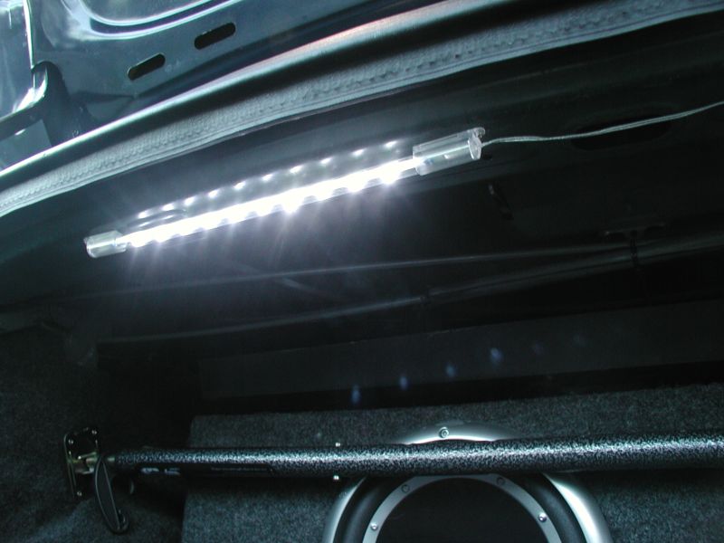 White LED strip light mounted under trunk lid illuminating carpeted trunk and subwoofer