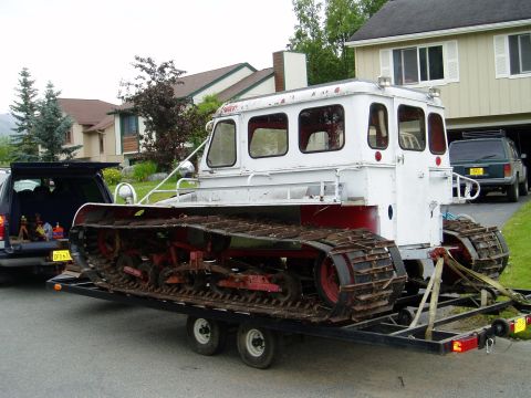 2000 Ford E350 - A tracked snow vehicle is being transported on a trailer behind a dark SUV, with houses in the background.