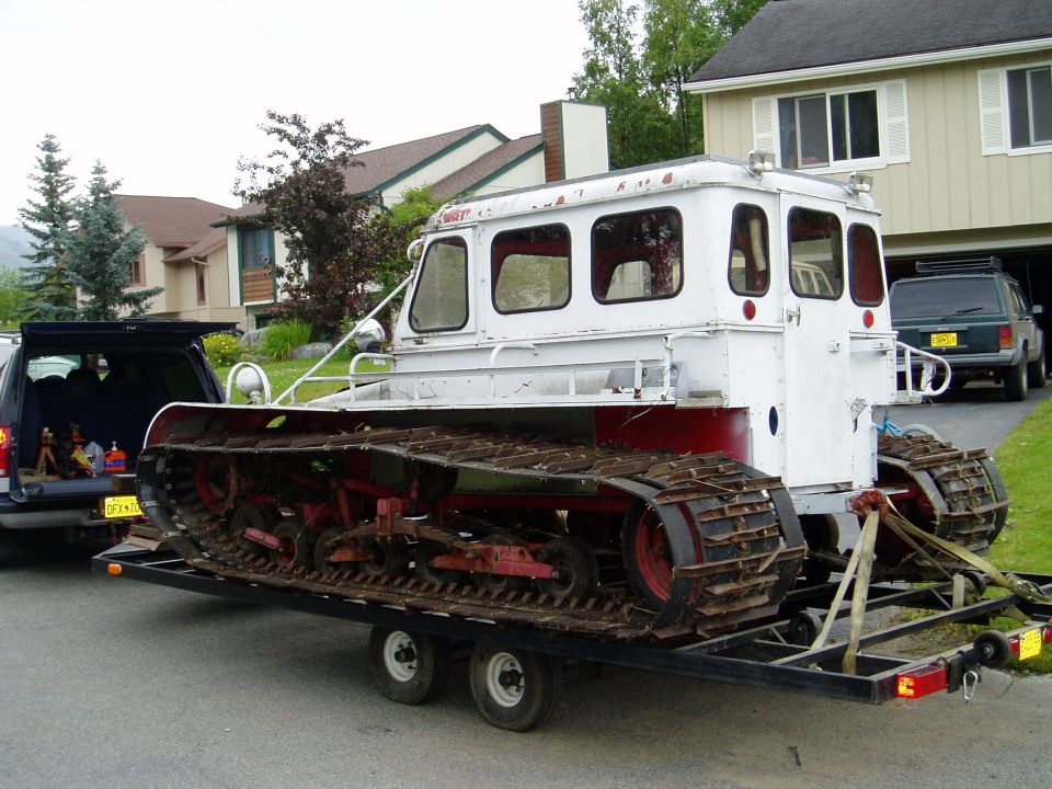 White and red tracked snow vehicle on a trailer, towed by an SUV