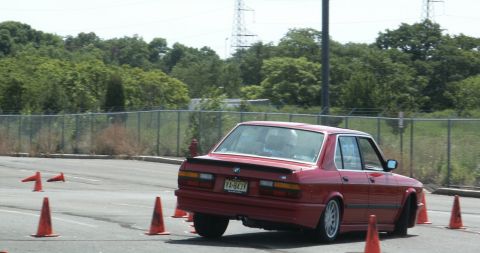 2001 Mercury Grand Marquis - A red BMW E28 sedan navigates an autocross course with orange cones marking the path.