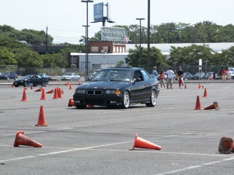 2001 Mercury Grand Marquis - A black BMW E36 coupe is seen on an autocross course, maneuvering around orange cones.