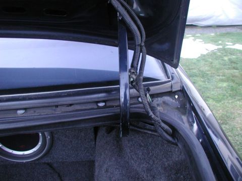 1990 Ford Thunderbird - The trunk of a 1990 Ford Thunderbird, showing the interior carpeting, a subwoofer, and the trunk lid hinge mechanism.