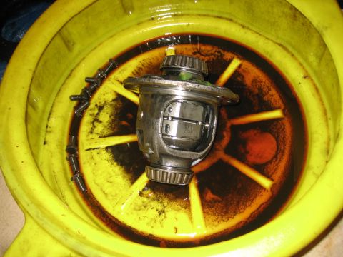2001 Jeep Wrangler - A differential carrier and several bolts are submerged in dark fluid within a yellow drain pan.