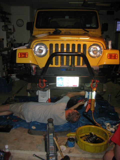 2001 Jeep Wrangler - A person works on the underside of a yellow Jeep Wrangler, likely performing maintenance or an upgrade.