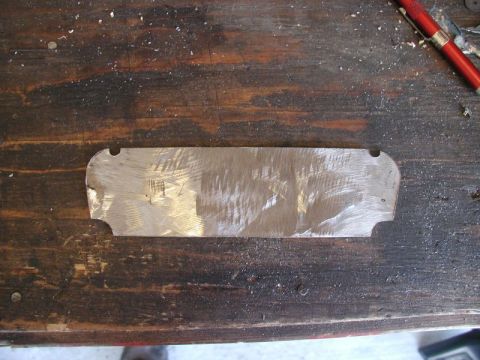 1990 Ford Thunderbird - A metal plate with a brushed finish lies on a wooden workbench, possibly awaiting installation or repair.