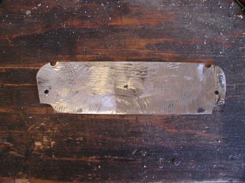 1990 Ford Thunderbird - A scratched metal plate with two mounting holes sits on a wooden surface.