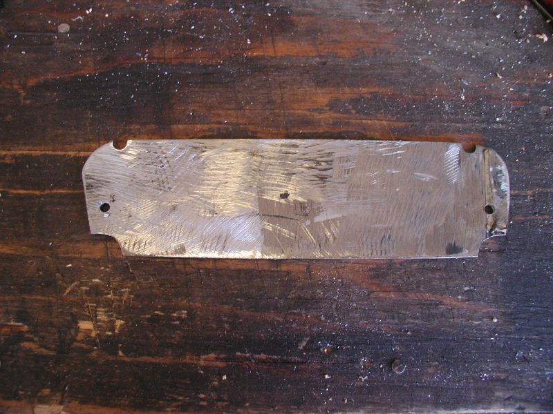 Bare aluminum switch panel blank with drilled holes on a dark wood workbench