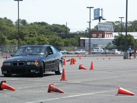 2001 Mercury Grand Marquis - A black BMW E36 coupe navigates an autocross course marked by orange traffic cones on a sunny day.