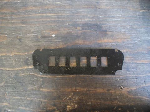 1990 Ford Thunderbird - A black metal panel with six rectangular openings, likely an interior car part, is shown against a wooden background.