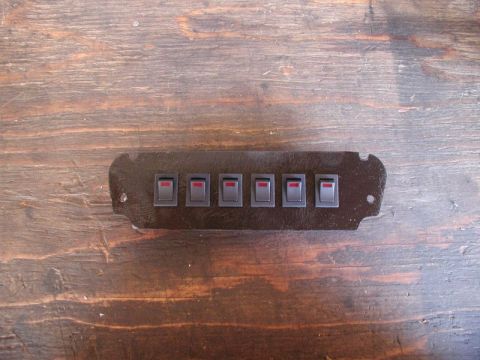 1990 Ford Thunderbird - A dark-colored ashtray switch panel six gray rocker switches with red indicator lights is shown against a wooden background.