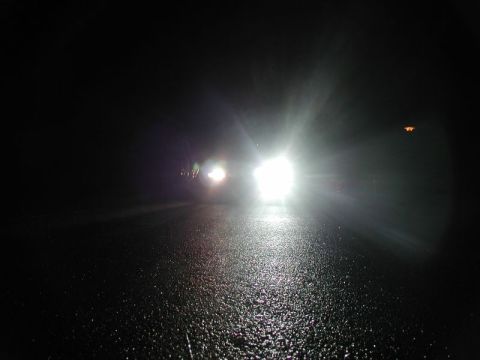 1990 Ford Thunderbird - Headlights illuminate a wet road at night as two vehicles approach.