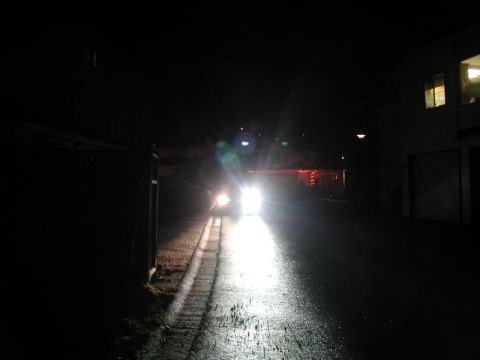 1990 Ford Thunderbird - A car's headlights illuminate a wet road at night, with a house visible on the right.