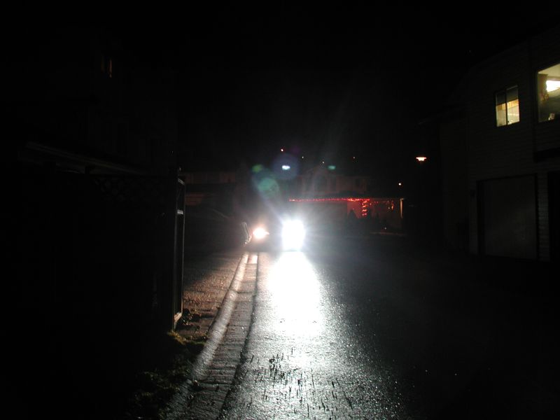 Car with bright headlights on at night, facing forward on a wet road