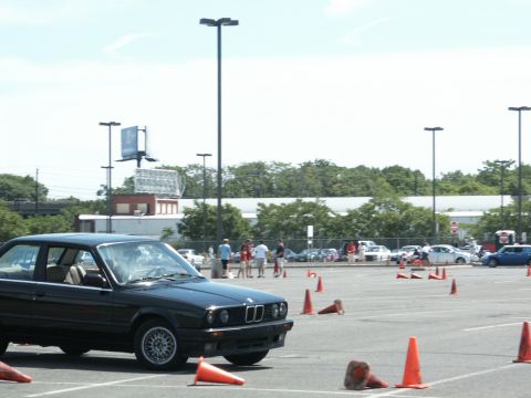 2001 Mercury Grand Marquis - A black BMW E30 coupe is parked in a lot during an event with several other vehicles and people in the background.