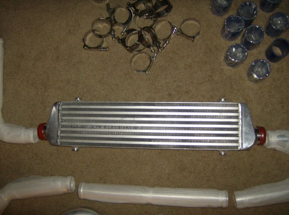 Intercooler with red fittings, wrapped piping, and metal clamps on a carpeted surface